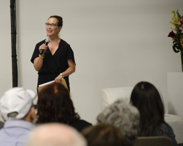 Christine Jowers holds a microphone and talks to an audience during an Enthusiastic Event!